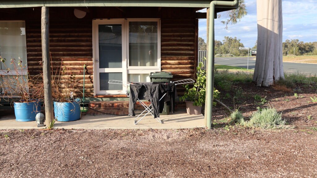 A small drying airer on the front verandah of a timber house, beside potted plants