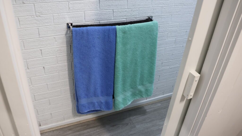 Two bath towels, one blue and one green, hanging on a rail against a white brick bathroom wall