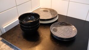 Small stacks of plates and black bowls on a kitchen bench, cut back by slow decluttering to the number used between washes