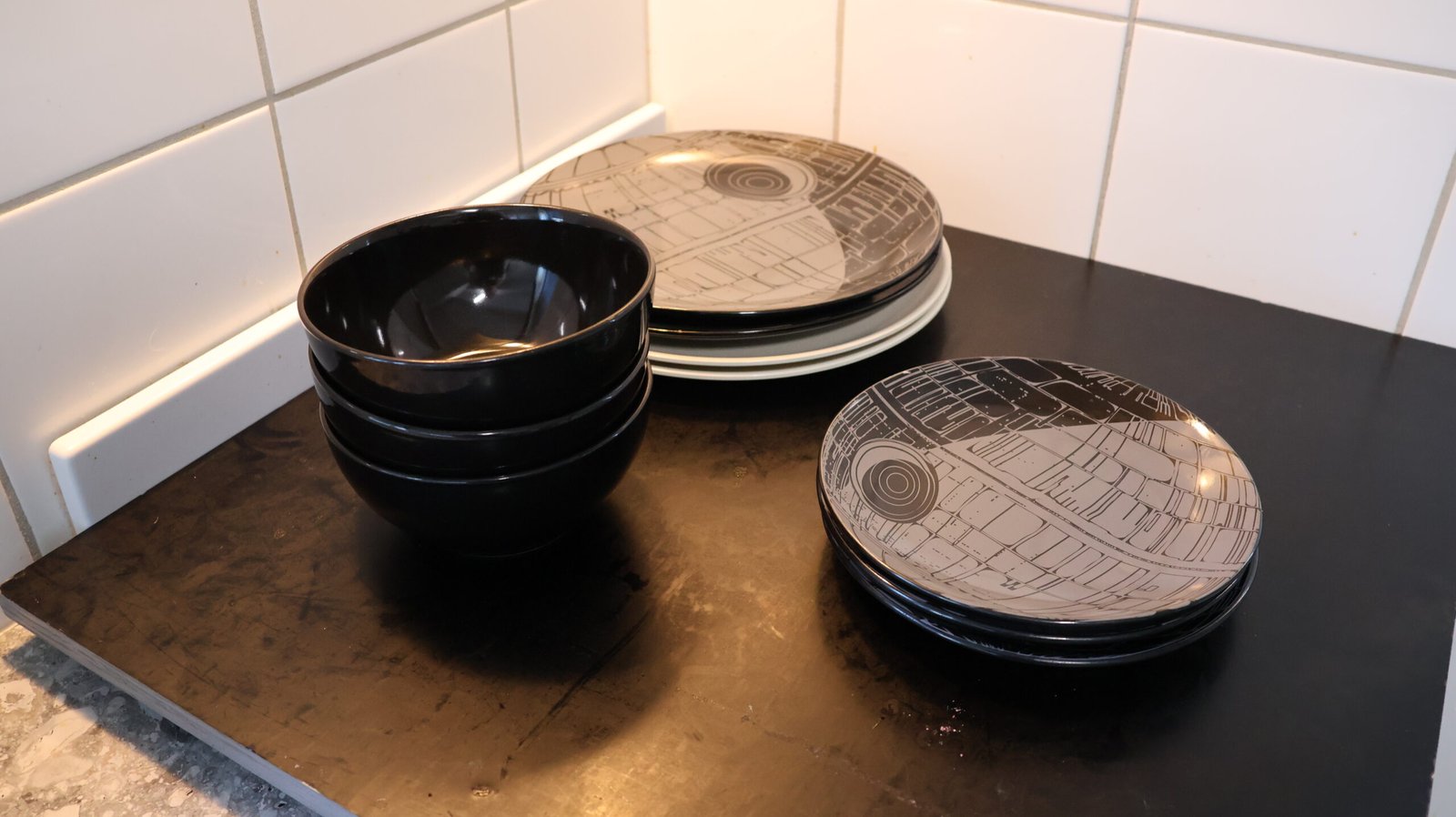Small stacks of plates and black bowls on a kitchen bench, cut back by slow decluttering to the number used between washes