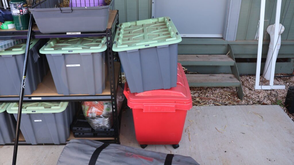 A metal shelving unit moved outside, now holding storage tubs of garden and BBQ gear