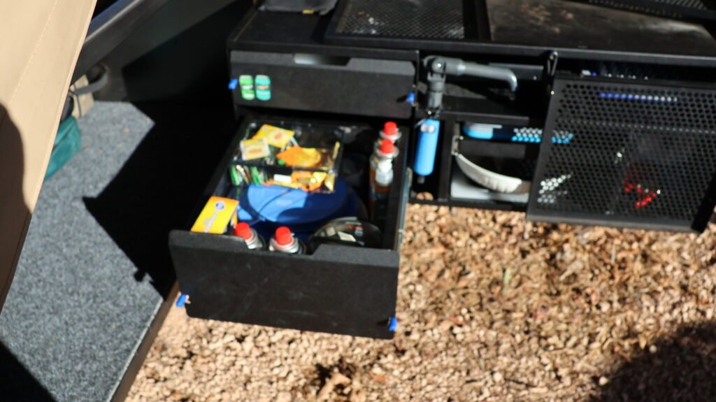 A slide-out drawer in a camper trailer, packed with everyday kitchen and cleaning items from the house